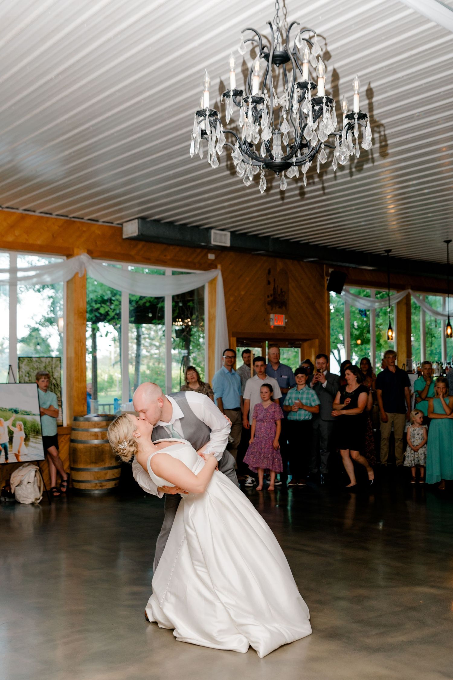 Bride and groom share a romantic dip kiss on the dance floor under a chandelier at their wedding reception.