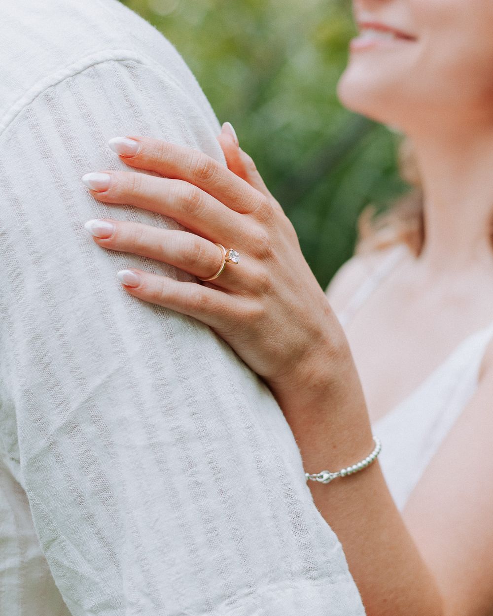 Close-up of a hand with engagement ring and bracelet resting on white fabric.