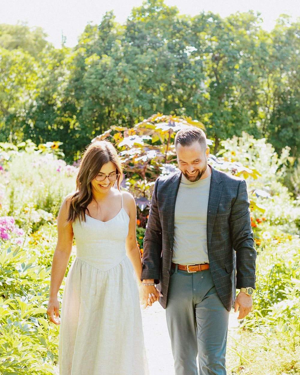 Couple walking hand in hand through a vibrant summer garden with sunflowers.