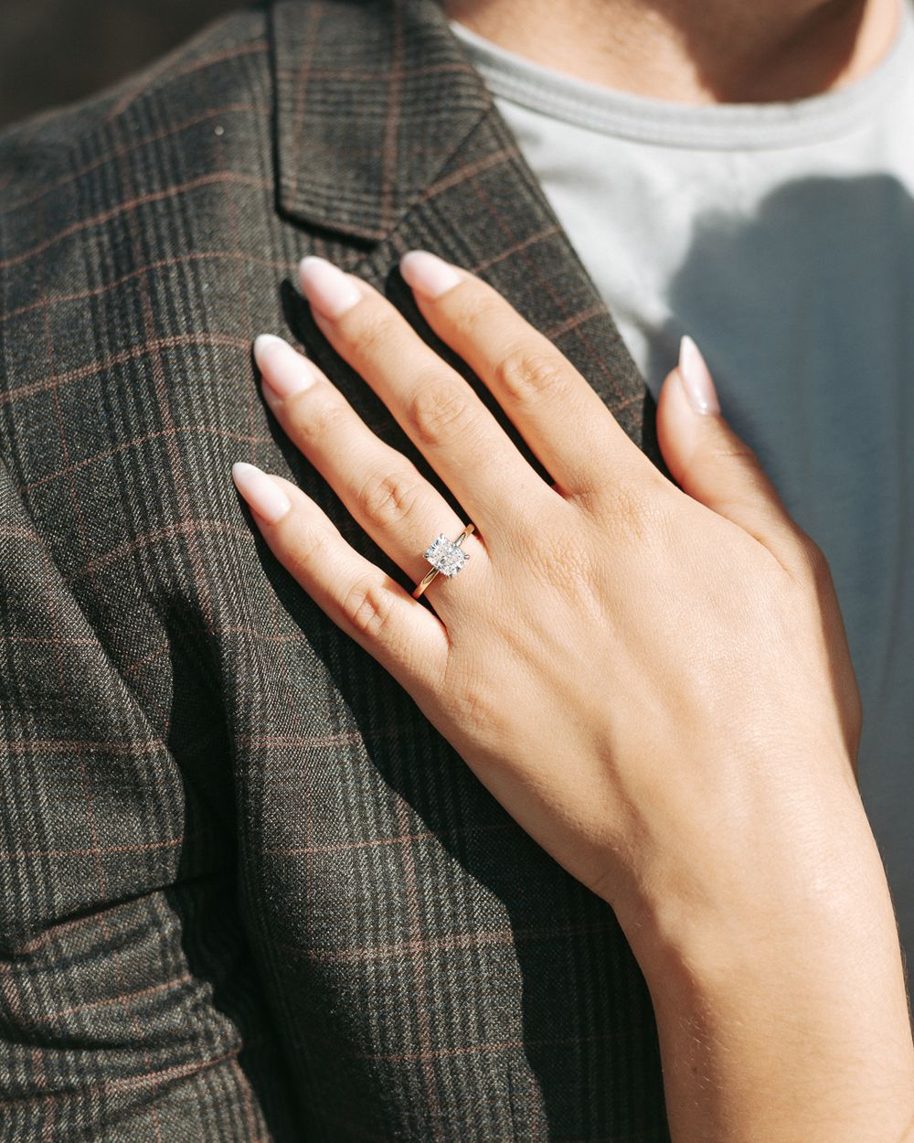Close-up of an engagement ring on a hand resting against a plaid jacket.