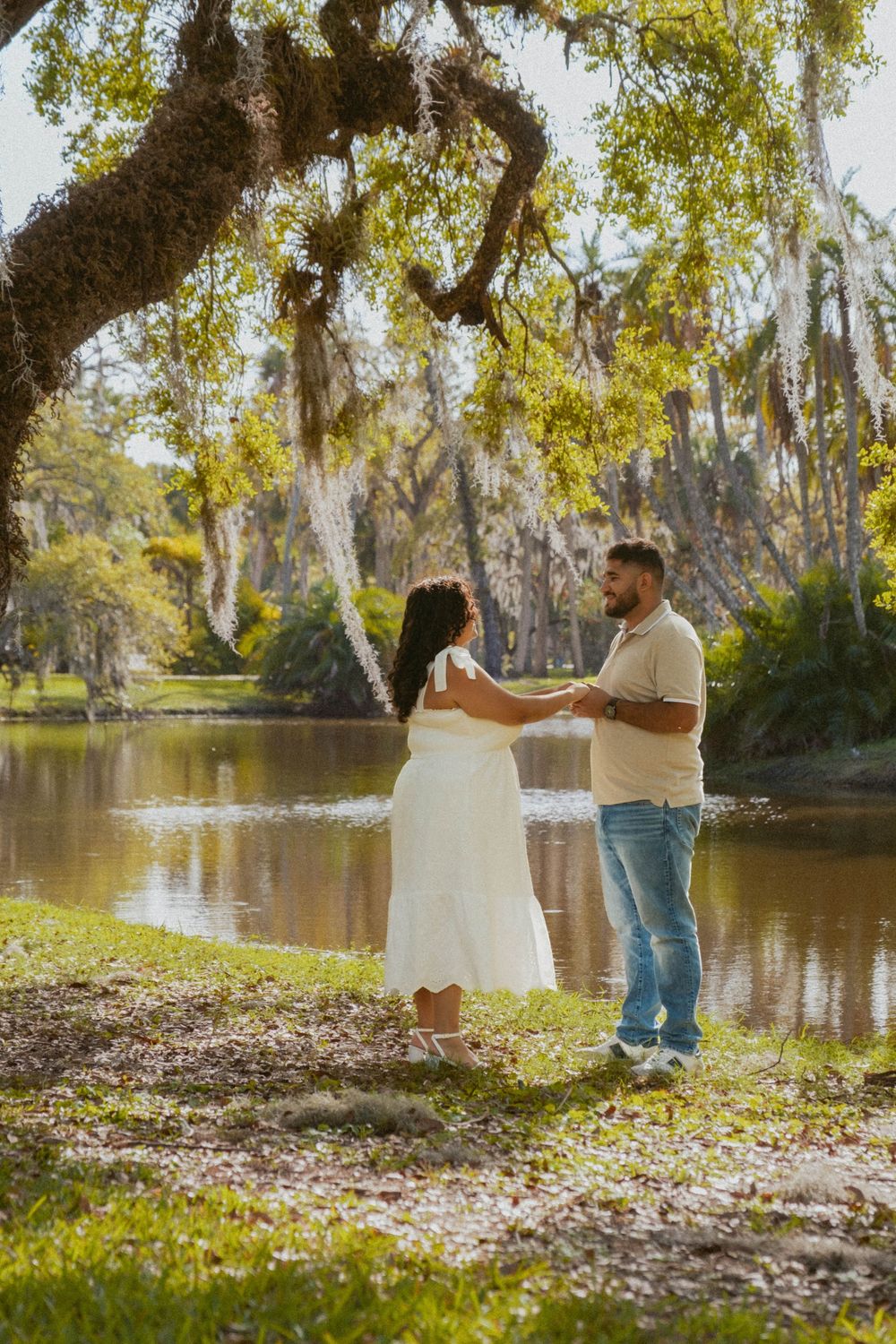 A couple shares a romantic moment by a scenic lake with Spanish moss hanging from trees.