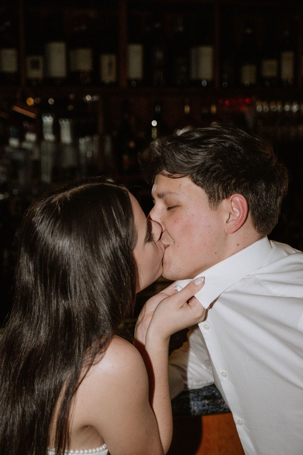 An intimate moment captured in a dark bar setting with bottles lining the shelves.