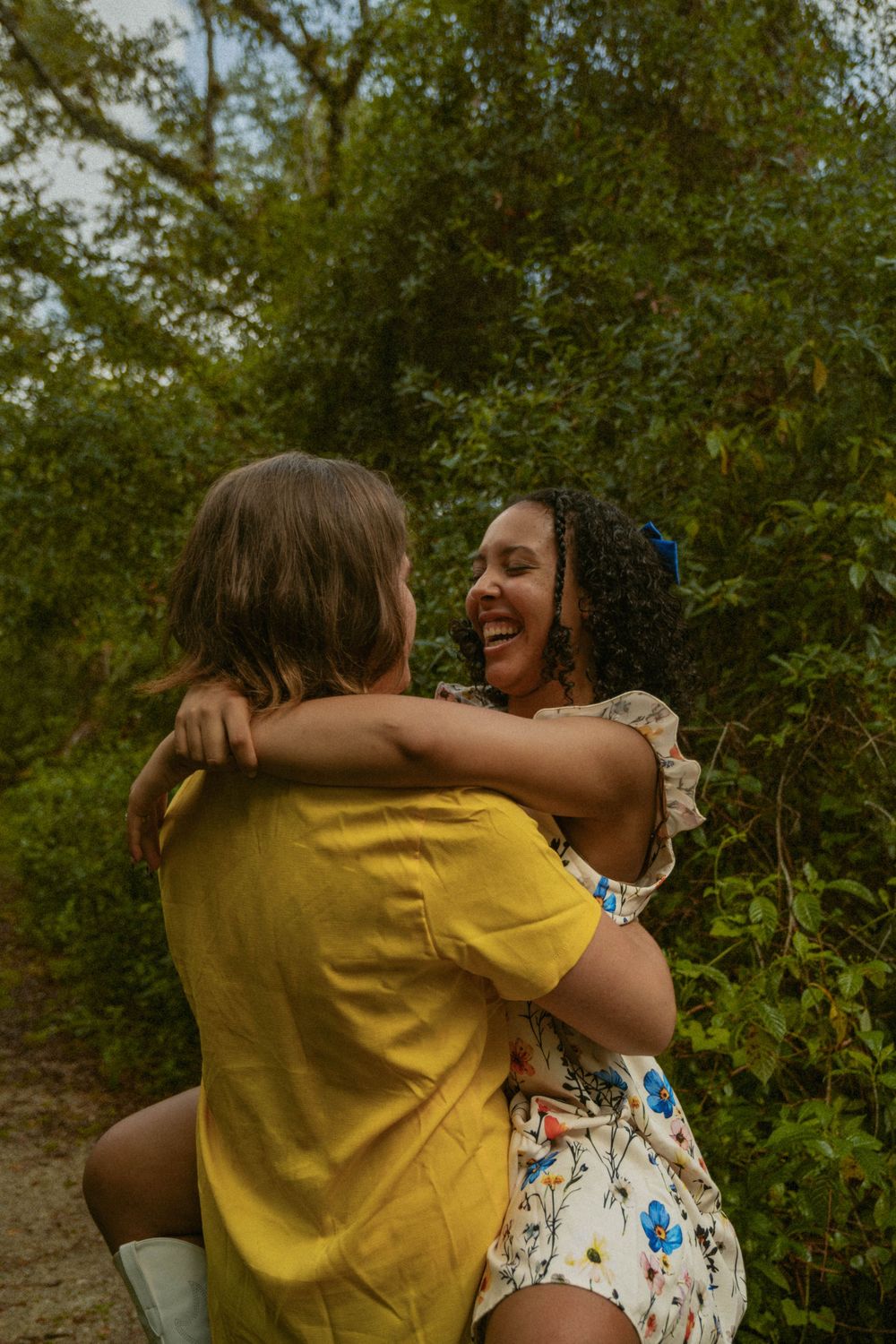 A joyful couple embraces outdoors surrounded by green foliage.