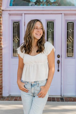 A series of fashion poses showing a white ruffle top paired with light wash jeans against a pink brick backdrop.