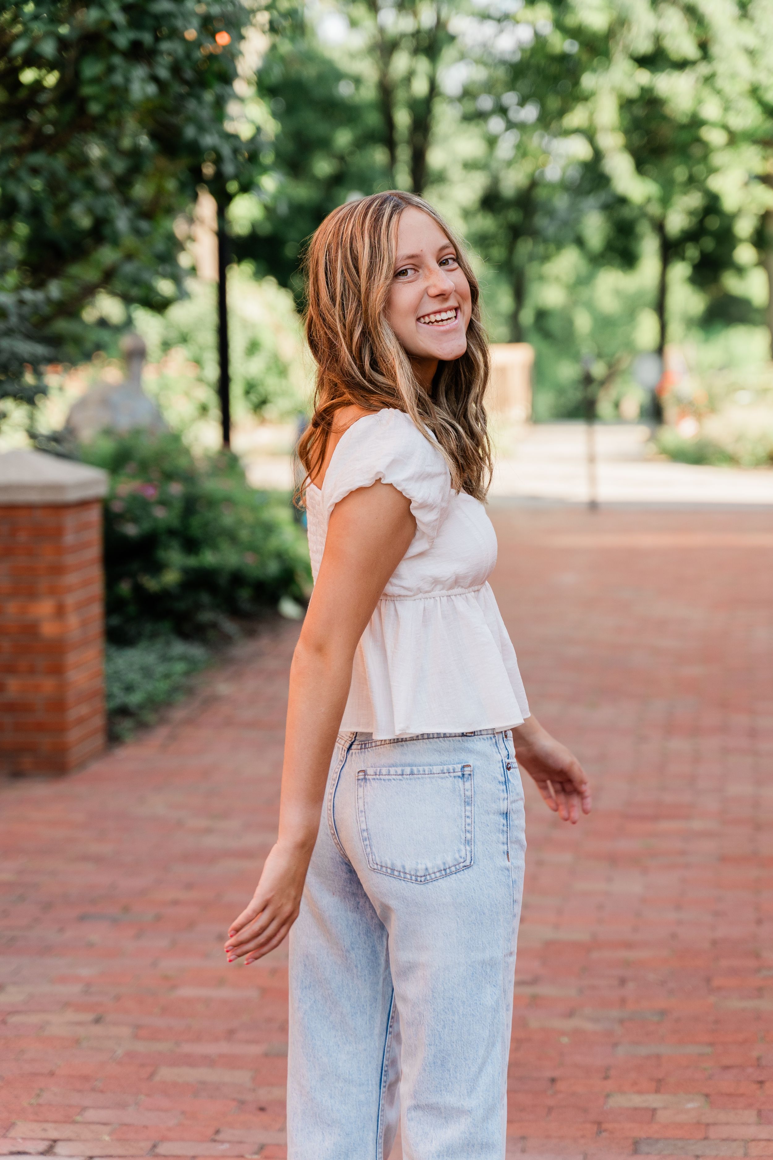 A casual summer outfit featuring a white sleeveless top and light denim photographed on red brick pavement.