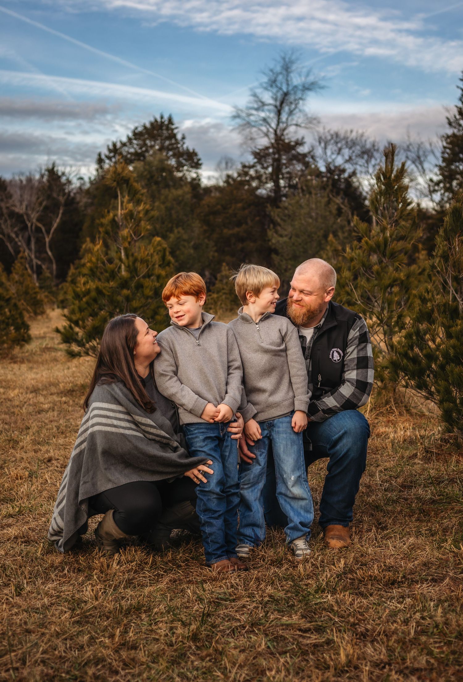A mother and father smile with their two boys against a Christmas tree farm backdrop, captured by Charlottesville family photographer.