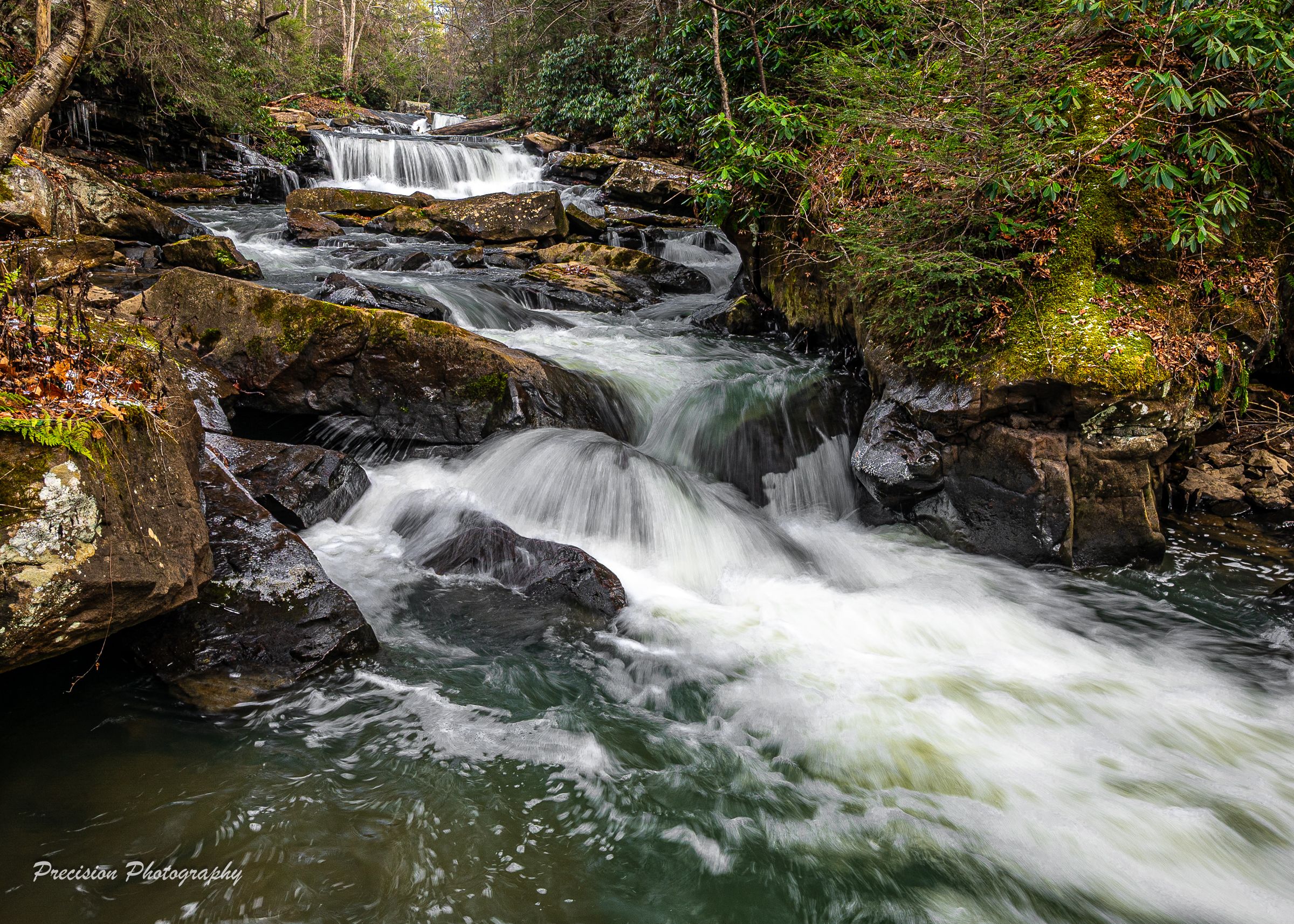 Cascading waterfall flows through moss-covered rocks in a lush forest setting.