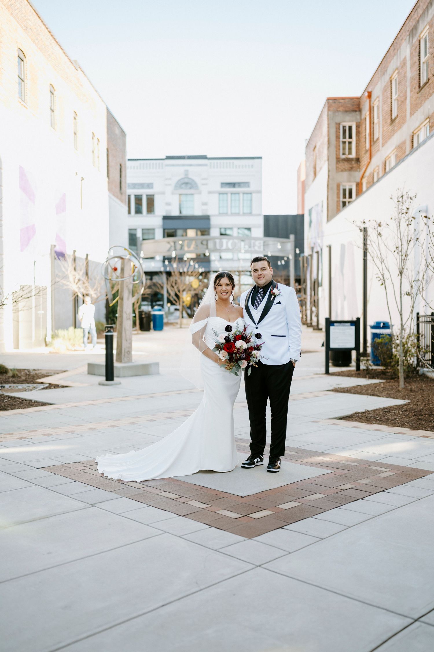 A couple shares a romantic moment while walking along a modern building courtyard with concrete pathways.