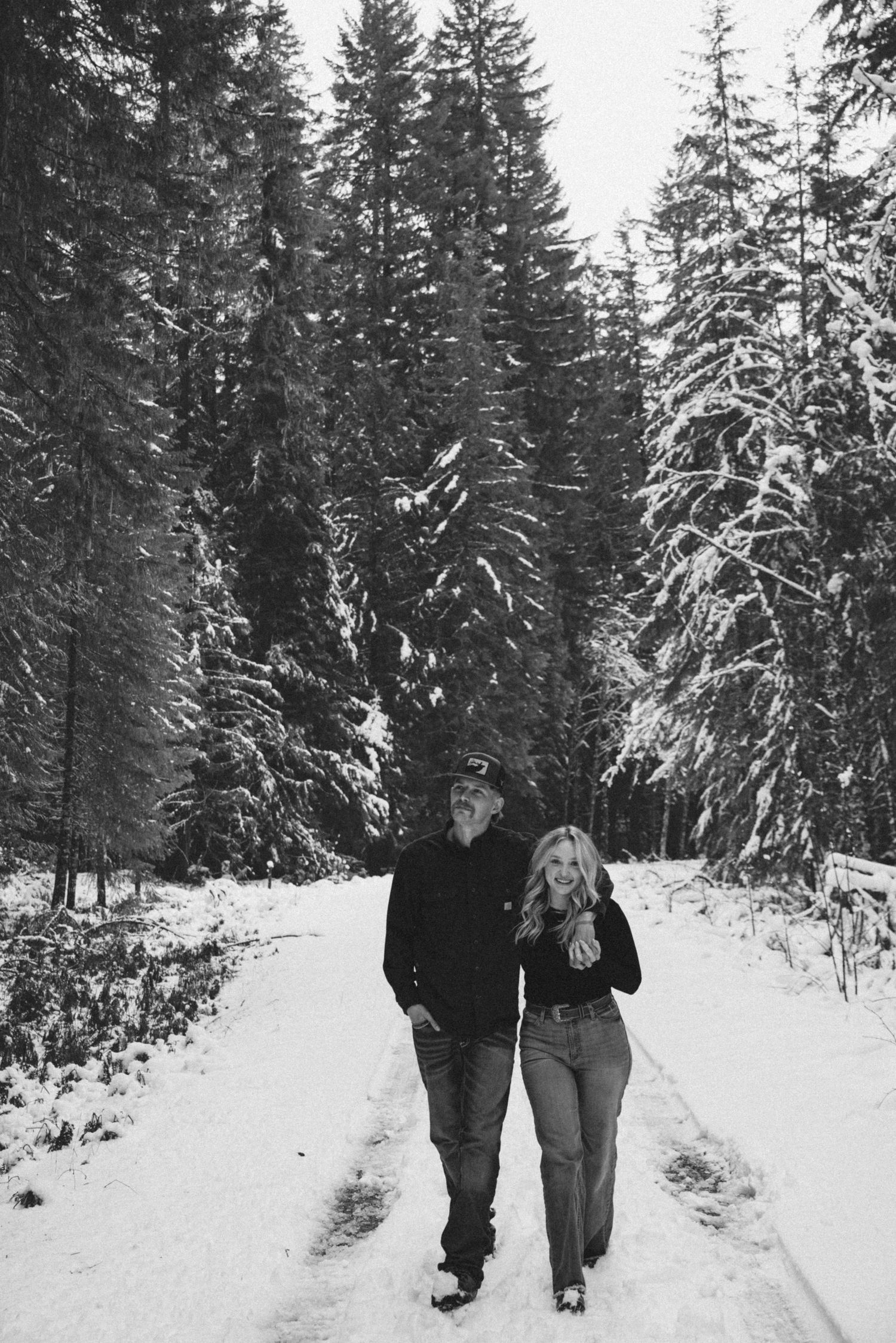 A snowy forest path with evergreen trees and people walking together in winter conditions.