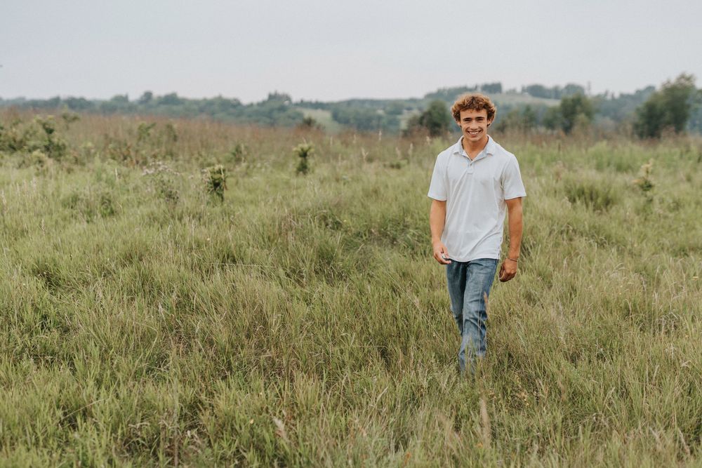 Person walking through tall grass meadow in rural countryside setting.