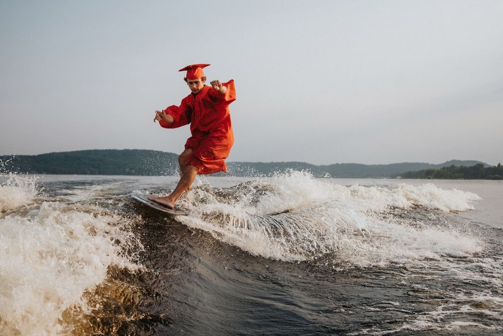 Surfer in red wetsuit rides wave across lake at sunset creating dramatic spray patterns.