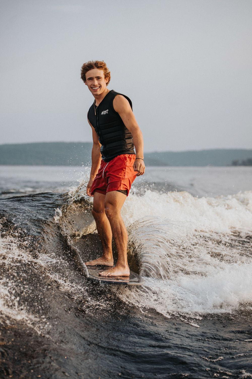 Person wakesurfing on a lake during sunset, creating splashes while riding the wake wave.