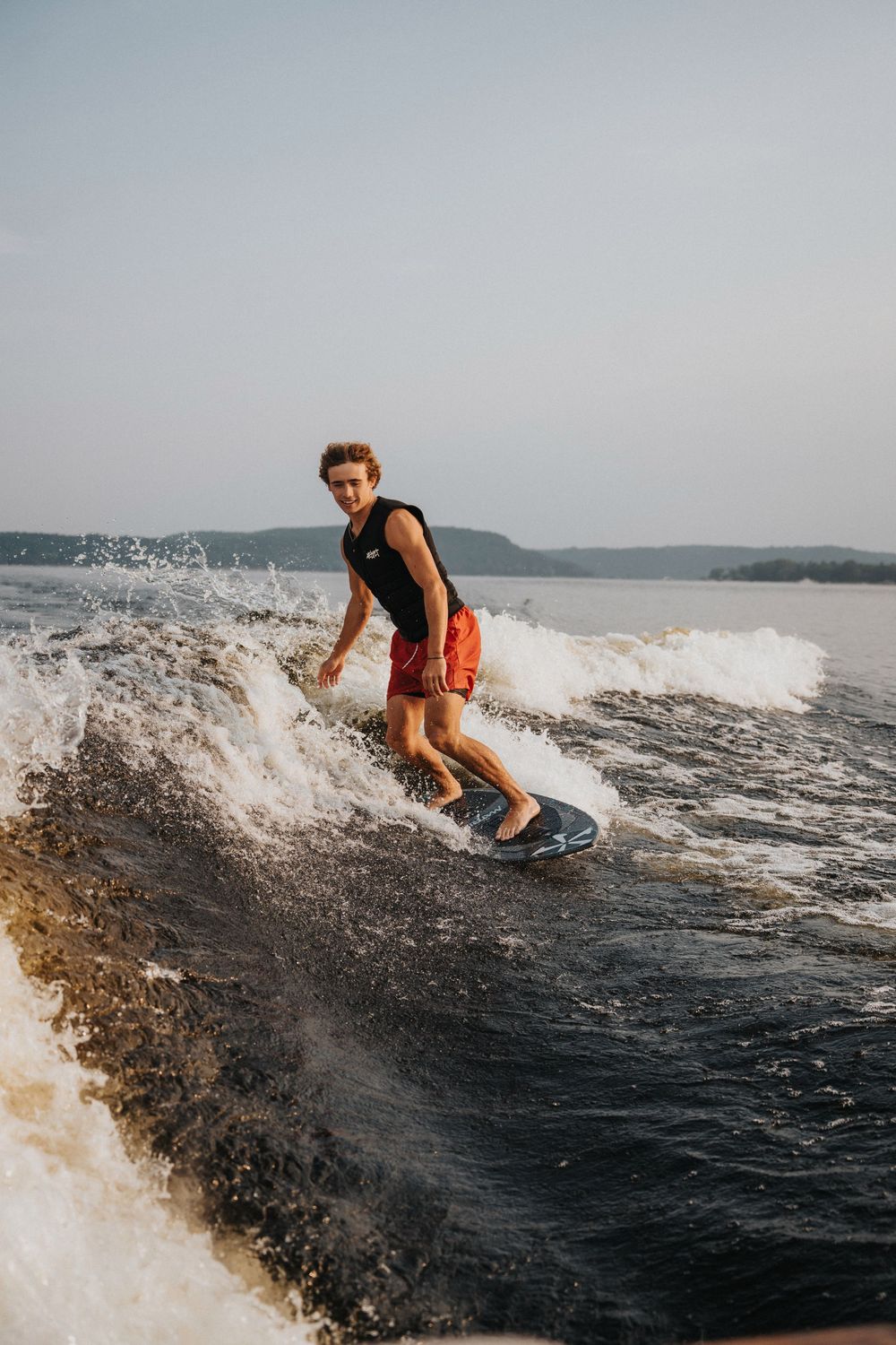 Dynamic shots of wake surfing behind a boat with water splashing on a sunny day.