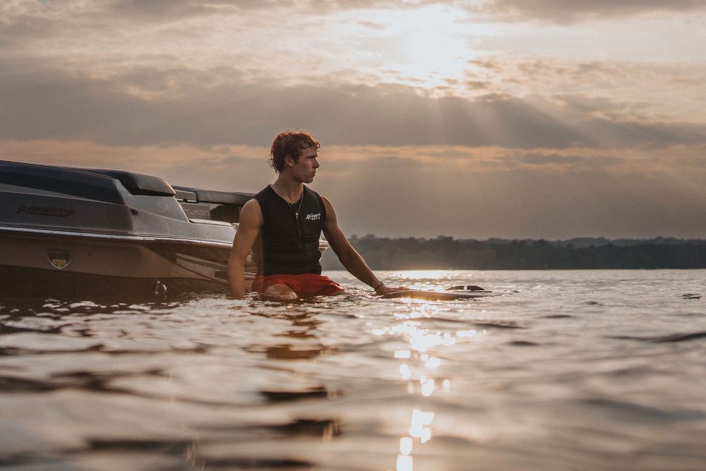 Silhouetted wake surfer gliding across calm water during golden hour sunset.