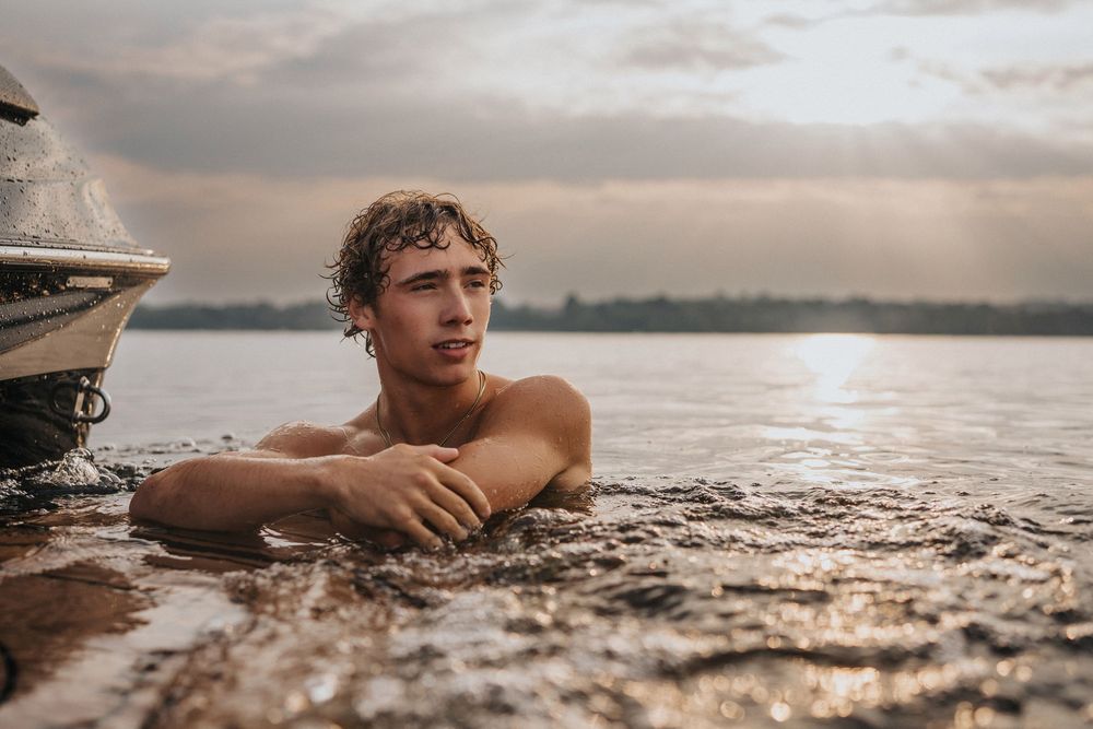 Person swimming in calm water at sunset with a serene landscape in the background.