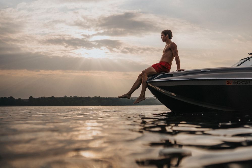 Silhouette of person sitting on edge of boat during sunset on calm waters.