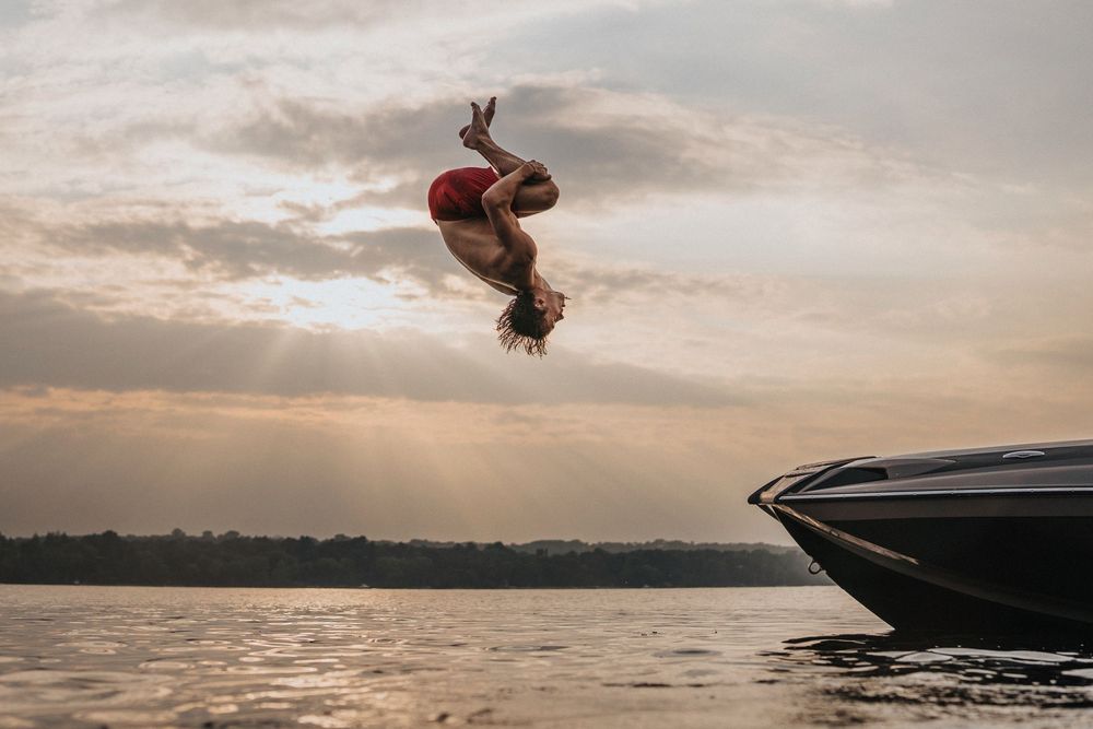 Silhouette of graduate performing backflips against dramatic sunset sky over water.