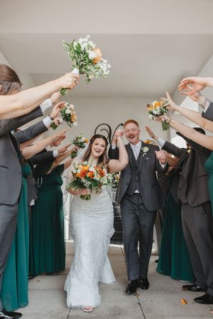 Wedding party in emerald green dresses and gray suits toasts with champagne glasses.