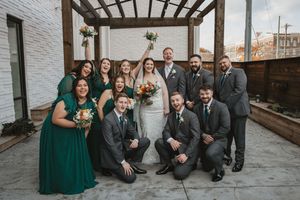 Wedding party in emerald green and grey poses together in urban setting.