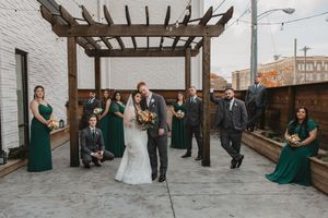 Wedding party poses under a wooden pergola with bridesmaids in emerald green dresses.