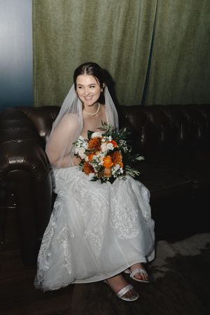 Wedding dress details and floral bouquet with orange and white flowers.