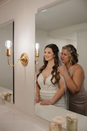 Getting ready moments in an elegant room with gold wall sconces and mirrors.