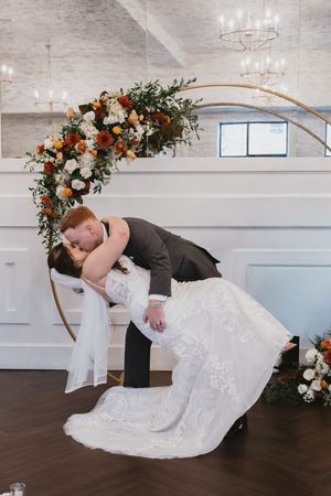 Creative wedding photography with couple posing against white brick wall and floral arch.