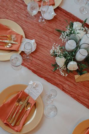 Elegant table setting with coral linens, gold chargers, and delicate floral centerpieces.