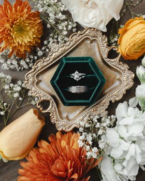 Wedding ring display with orange dahlias and white flowers on ornate vintage tray.