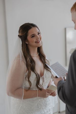 Bride in lace gown reads from paper during wedding ceremony.