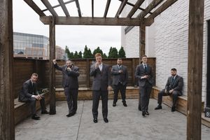 Wedding party poses under wooden pergola structure during outdoor photo session.