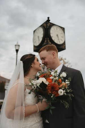 Intimate wedding portraits captured against an overcast sky featuring orange and white floral arrangements.