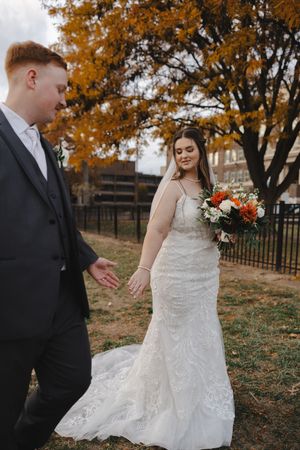 Autumn wedding photoshoot with couple walking through fallen leaves and orange trees.