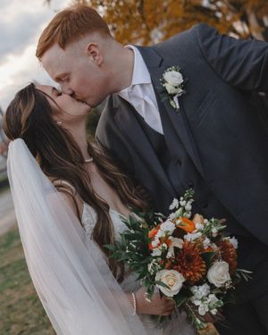 Autumn wedding portrait with bride holding orange and white floral bouquet during outdoor ceremony.