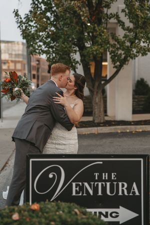 Romantic wedding couple shares a kiss in front of The Ventura venue sign during an outdoor autumn photo session.