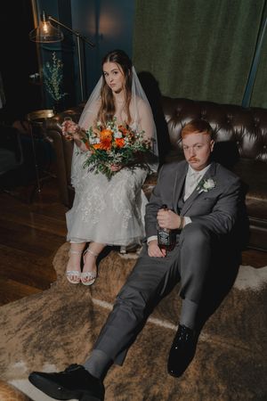 Couple relaxing on leather couch during wedding reception with autumn decor.