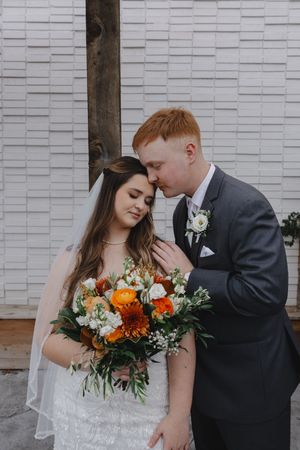 Romantic wedding portraits against white brick wall with orange and white floral bouquet.