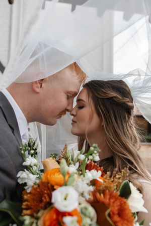 Romantic wedding portrait with orange and white bouquet under flowing veil.