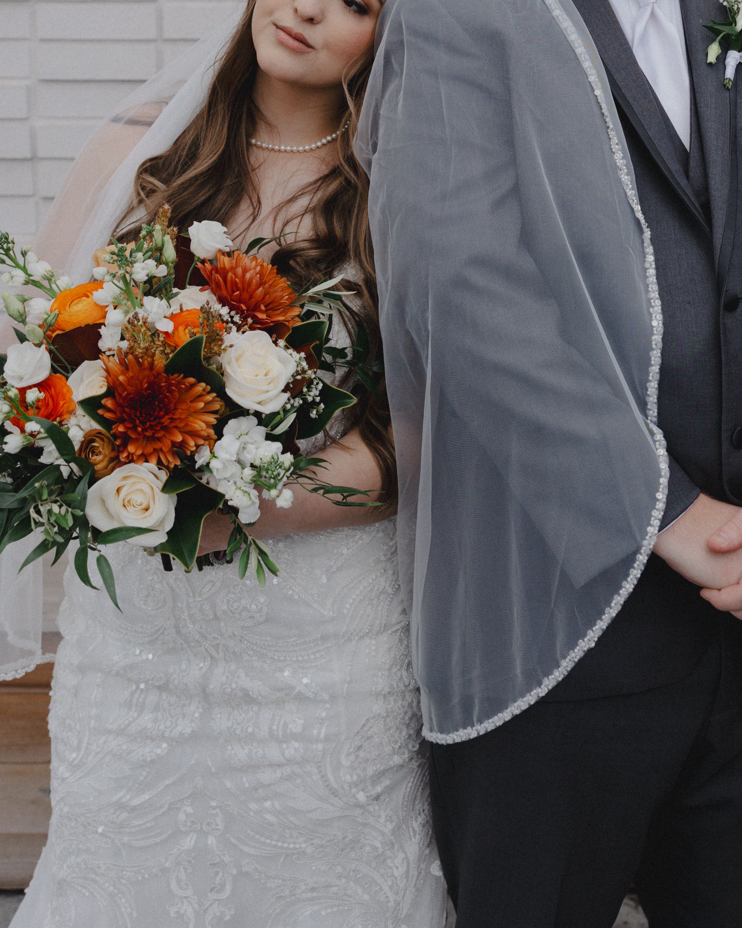 Elegant wedding portrait featuring bride in lace dress with orange and white floral bouquet.