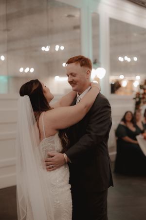 Couple shares their first dance in an elegant white reception hall with glowing chandeliers.