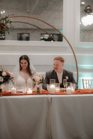 Wedding reception table setup with modern copper arch decor and glowing candles creating an intimate atmosphere.