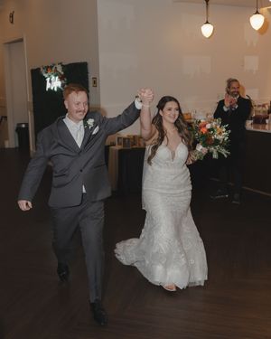 Wedding couple dances joyfully across a reception hall floor in classic formal attire.