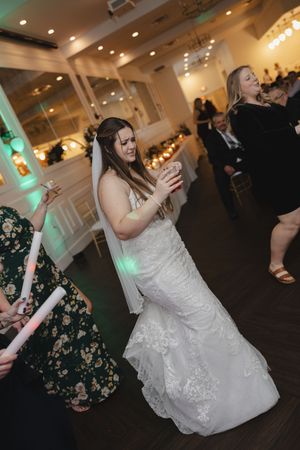 Wedding reception guests dance and celebrate on a dark wooden dance floor with ambient lighting.