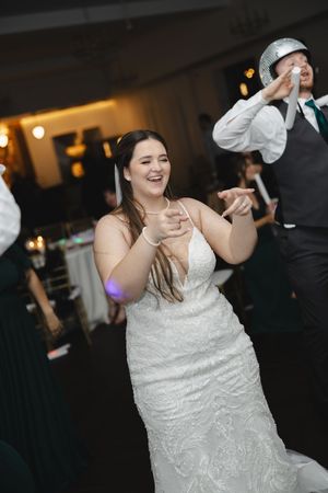 Wedding reception dance floor scene with bride in white lace dress celebrating joyfully.