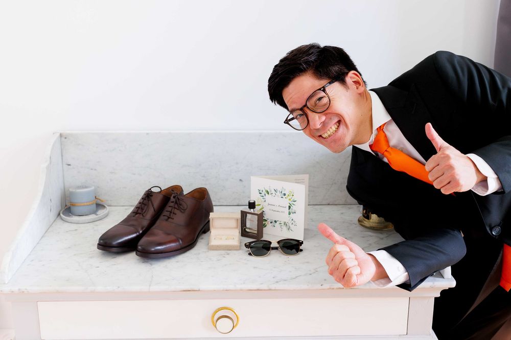 Wedding preparation display showing brown dress shoes, colognes and accessories on white shelf.