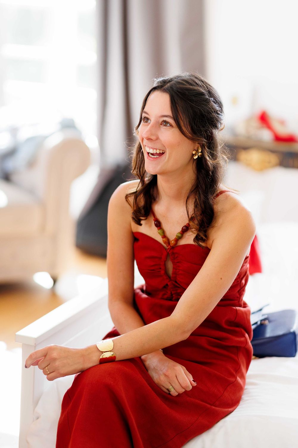Woman in red formal dress sitting and smiling in elegant interior setting.