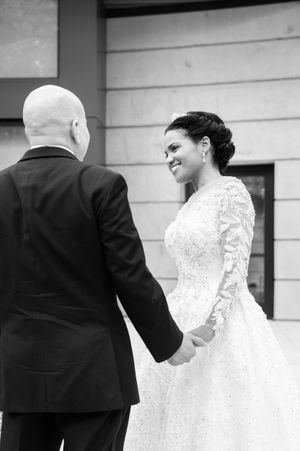 A black and white wedding photo captures a couple in formal attire walking together outdoors.