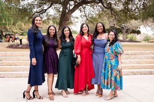 A group in formal dresses standing together on outdoor stone steps in coordinated colors.