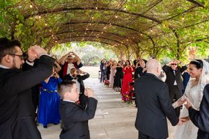 Wedding guests dance and celebrate together under a covered outdoor venue during a reception celebration.