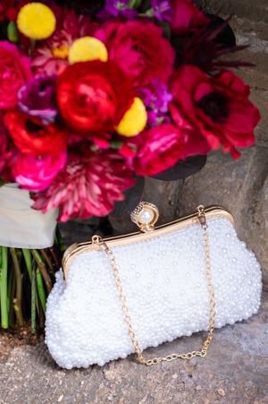 White beaded clutch purse displayed with vibrant red and pink floral arrangements.